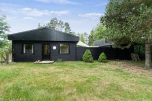 ein schwarzes Haus mit zwei Bäumen im Garten in der Unterkunft Ferienhaus In Der Nähe Eines Schönen Sandstrandes in Gedser + 14 Fotos