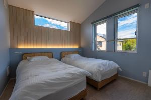 two beds in a bedroom with two windows at RYOAN Ichinomiya in Ichinomiya