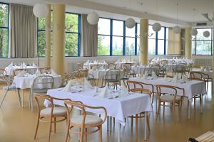 a room with white tables and chairs and windows at Hotel SOREA MORAVA in Tatranská Lomnica