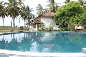 a swimming pool in front of a house with palm trees at Coconut Grove Beach Cabanas in Hungama