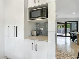 a kitchen with white cabinets and a microwave at Nerita Nook in Nelly Bay +13 photos