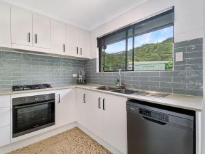 a kitchen with white cabinets and a sink and a window at Nerita Nook in Nelly Bay