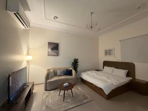 a bedroom with a bed and a chair and a tv at شادن للوحدات السكنية in Qufār