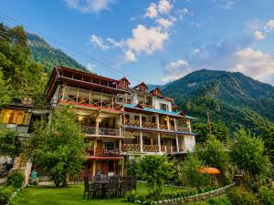 a large building with tables and chairs in front of a mountain at Sneha Riverside Cottage, Tirthan Valley - Best selling cottage in Jibhi 2025-26 in Jibhi