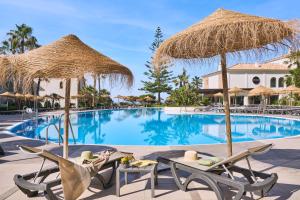 a resort pool with two chairs and umbrellas at Barceló Punta Umbría Mar in Punta Umbría