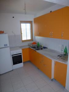eine Küche mit orangefarbenen Schränken und einem weißen Kühlschrank in der Unterkunft Apartments Kujundžić in Kaprije