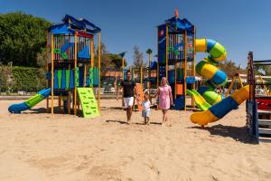 a man and a woman and child walking through a playground at Camping Village Garden Paradiso in Cavallino-Treporti