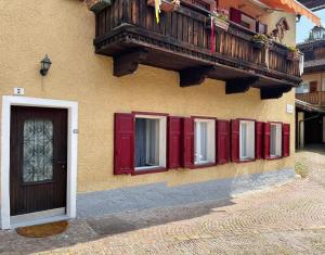 a building with red doors and a wooden balcony at Casa Christa in Castello di Fiemme