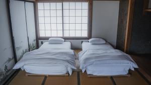 two twin beds in a room with a window at ゲストハウス麓〼-Rokumasu in Yokooka