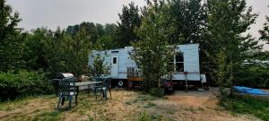 a white caravan in the woods with a table and chairs at Le Refuge du Navigateur in Tadoussac