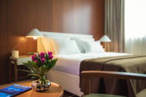 a hotel room with a bed with a vase of flowers on a table at Prima Millennium in Ra‘ananna