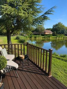 a wooden deck with two chairs and a lake at Swan cove - Lakeside Caravan Park in Denver +6 photos