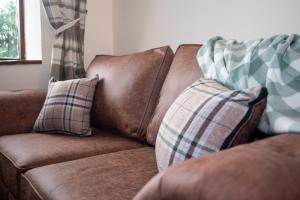 a brown leather couch with two pillows on it at Lake View - Old Mill Cottages in Ilfracombe