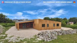 a wooden house on a beach with a field at Eksklusivt Luksusferiehus Med Pool Sj455 in Harboør
