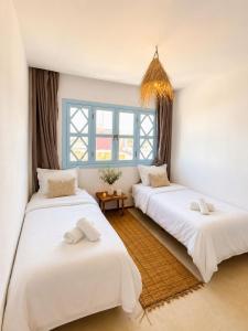 two beds in a room with two windows at Appartement LE SABLE Uniquement les familles in Oualidia