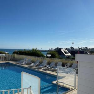 a swimming pool with chairs and a fence at BELLE VUE MER STUDIO PISCINE in Trévou-Tréguignec
