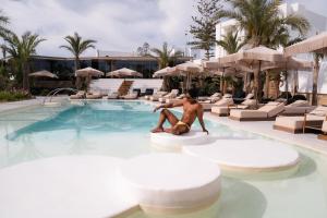 a man sitting on a surfboard in a swimming pool at Axel Beach Mykonos - Adults Only in Mikonos