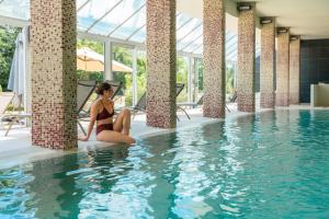 a woman in a bikini sitting in a swimming pool at Domaine des Dryades - Hôtel & Spa in Pouligny-Notre-Dame