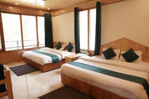 two beds in a room with windows at Hotel Mid Orchard Kasol -River Side in Kasol