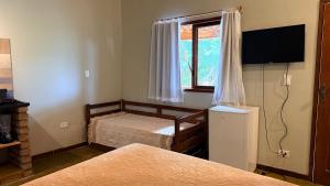 a bedroom with two beds and a television and a window at Vila Clara do Capão in Vale do Capao