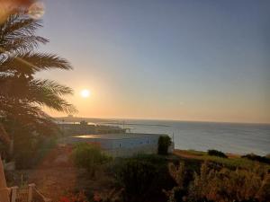 a sunset over the ocean with a building and a palm tree at Casa venere in Pachino