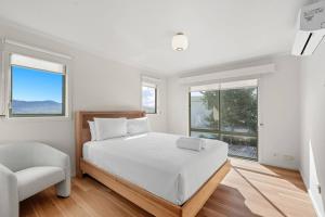 a bedroom with a bed and a chair and windows at Riverview Townhouse Retreat in Lindisfarne