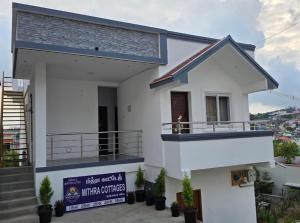 a white house with a balcony and a sign at Mithra Cottages individual Villa in Ooty