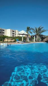 a swimming pool with blue water and a beach at Aghadir Village قرية اغادير in El Alamein