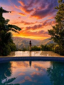 a person standing next to a swimming pool at sunset at Chamanica in Coroico
