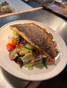 a white plate with a fish sandwich and a salad at The Ladybower Inn in Bamford