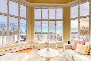 a living room with large windows and a table at Bayfront home with 270-degree views, large deck & porch - near Popham Beach in Phippsburg