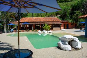 a swimming pool with an umbrella and a house at Hotel Rural Vale das Nascentes in Salesópolis