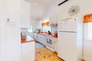 a white kitchen with white appliances and wooden floors at Waterfront home on St George River with private beach & deck - near festivals in Cushing +19 photos