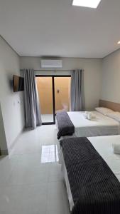 a bedroom with three beds and a tv and a window at Pousada Vila dos Anjos in Chapada dos Guimarães