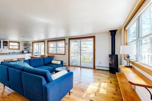a living room with a blue couch and some windows at Dog-friendly river-view home with wood stove, deck, patio, dock, beach, grill in Boothbay