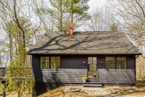 a small black house with a chimney on top at Renovated woodland home with lovely deck & firepit - minutes to Swan Lake in Swanville