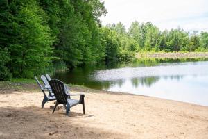 a bench sitting on the sand next to a lake at Chalet Essentiel 76 in Saint-Faustin