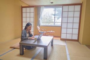 a woman sitting at a table with a laptop at ATAMI SPRING TERRACE HOTEL in Atami