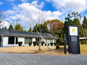 ein Schild vor einem Haus mit einem Baum in der Unterkunft FUWARI-kumamoto-12時チェックアウトでゆったり滞在 パターゴルフと絶景を楽しむ1日1組宿 in Aso