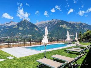 a pool with two chairs and umbrellas and mountains at Schenna Garni Eden Bed & Breakfast in Schenna