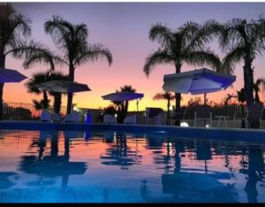 a swimming pool with umbrellas and chairs and palm trees at Villa Selinus 6598 in Castelvetrano Selinunte