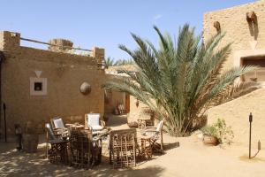 a patio with chairs and tables and a palm tree at Tanirt ecolodge in Siwa