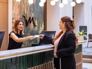 Eine Frau überreicht einer Kundin an einem Schalter eine Karte. in der Unterkunft Mercure Brussels Centre Rogier in Brüssel