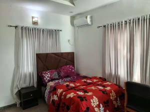 a bedroom with a red bed and white curtains at Naira and Kobo Hotel in Umuahia +1 photo