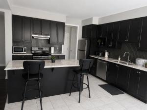 a kitchen with black cabinets and two bar stools at Cozy Beautiful Home in Brampton