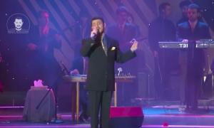 a man singing into a microphone on a stage at Hekmt home in Kafr al Ishārah