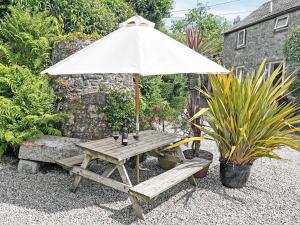 a wooden picnic table with an umbrella and a bench at Henwood Barn - Uk52138 in Liskeard