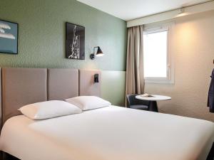 a bedroom with a white bed and a table and a window at ibis La Roche Sur Yon Vendespace in Mouilleron-le-Captif +184 photos