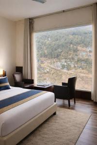 ein Hotelzimmer mit einem Bett und einem großen Fenster in der Unterkunft Tata Vista By Vaikunth - McLeod Ganj-Centrally Heated & Air Cooled # Near Mall Road # Big Parking # Lift #Spacious Rooms # Most Awarded # Property Of The Year # in Dharamshala + 75 Fotos