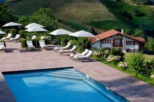 a swimming pool with chairs and umbrellas and a house at Auberge Ostapé in Bidarray